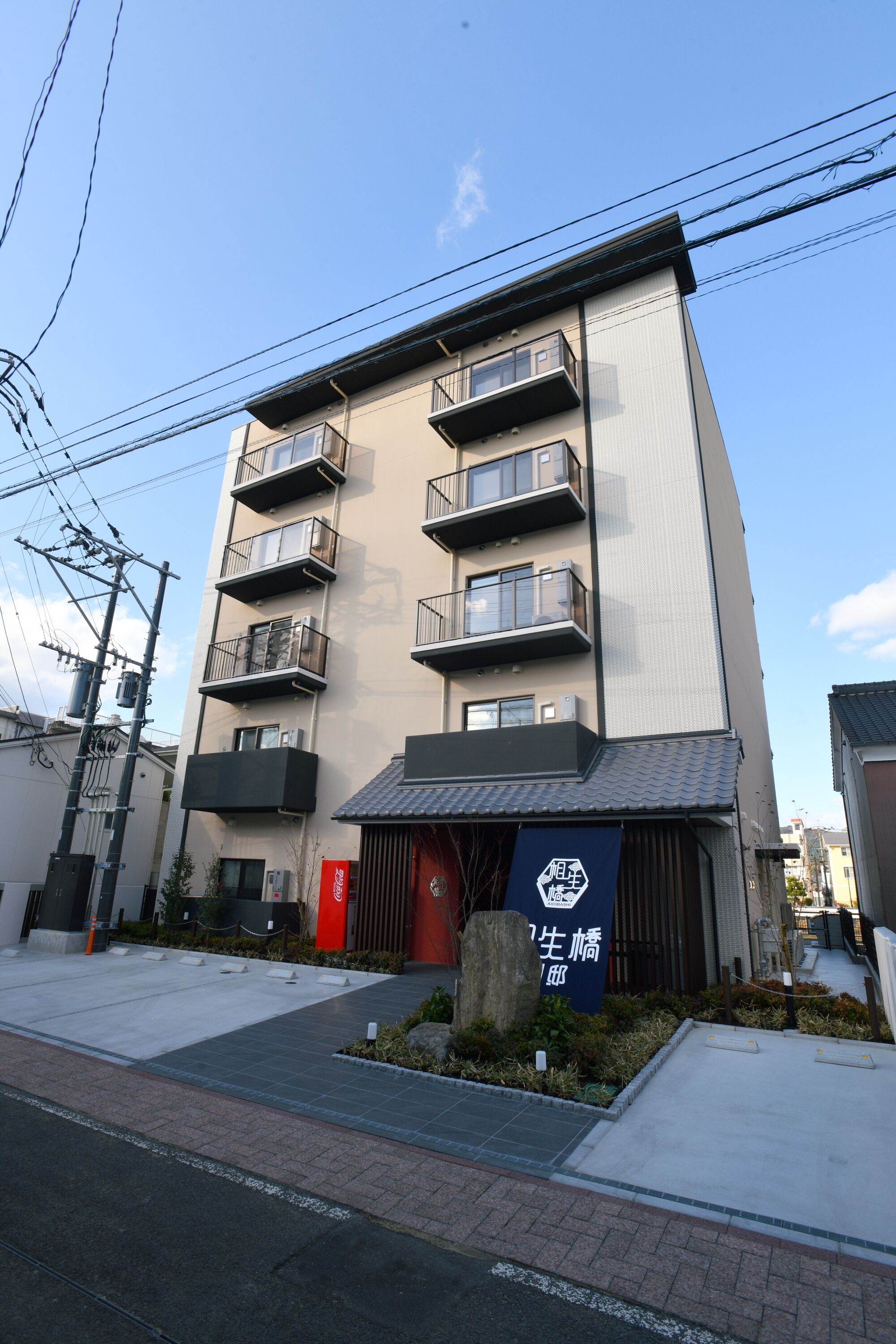 A multi-story building with balconies, a red entrance, and a sign with Japanese characters.