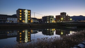 A calm river reflecting buildings, a bridge, and mountains in the background.