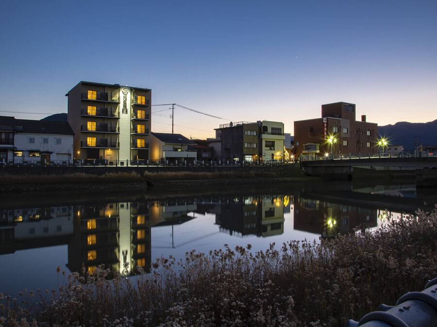 A calm river reflecting buildings, a bridge, and mountains in the background.