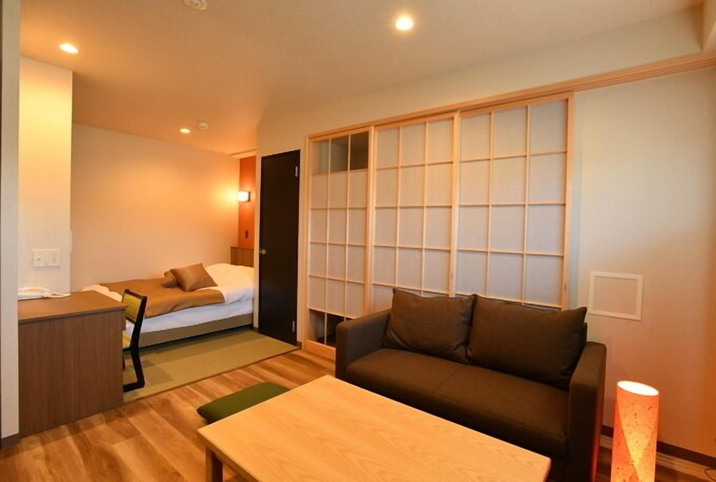 Een compacte hotelkamer met een bed, een sofa, een bureau en een schuivende shoji-scherm.