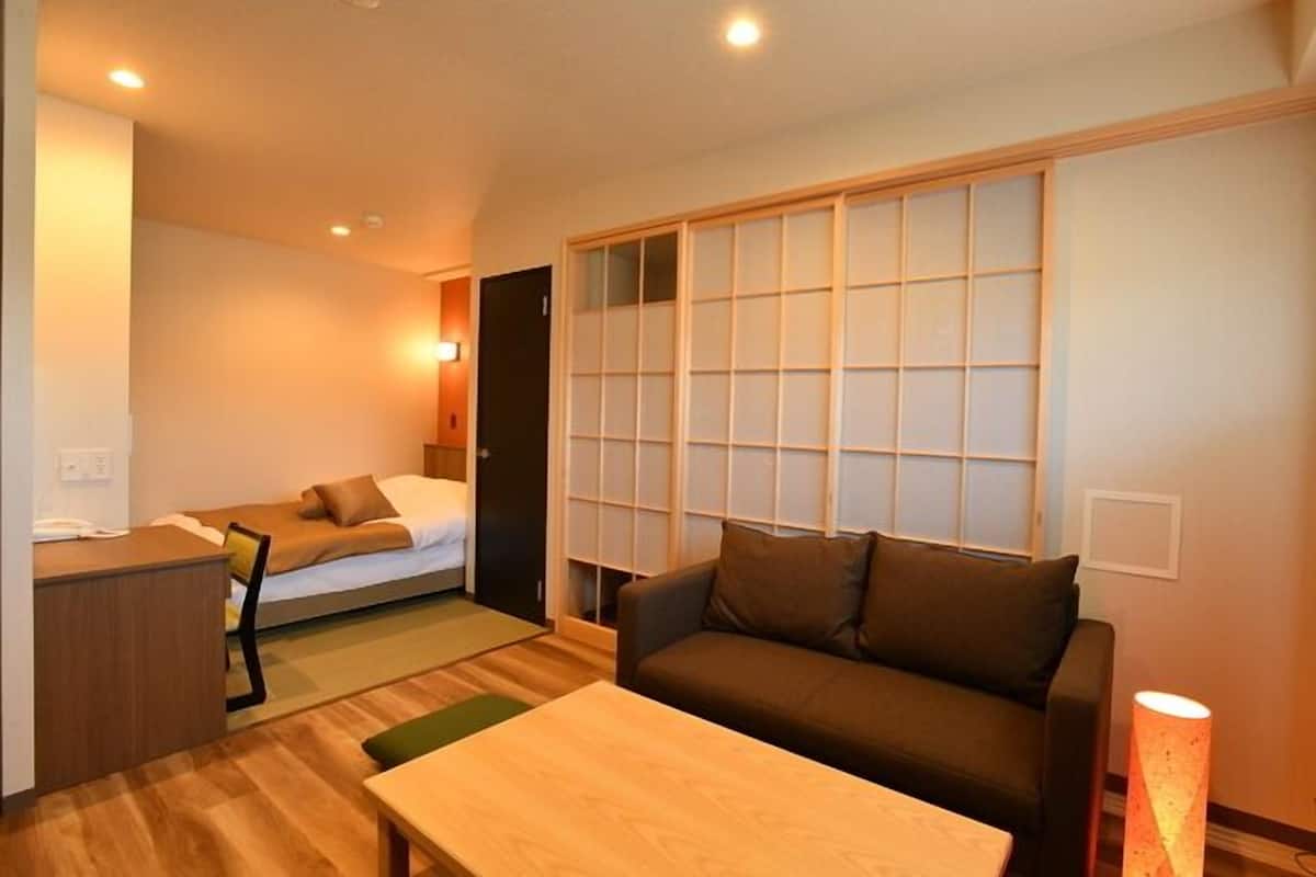 A compact hotel room with a bed, a sofa, a desk, and a sliding shoji screen.