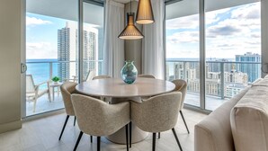 Un comedor moderno con una mesa redonda, cuatro sillas, un florero y lámparas colgantes. Cuenta con ventanas amplias con vista a la ciudad.