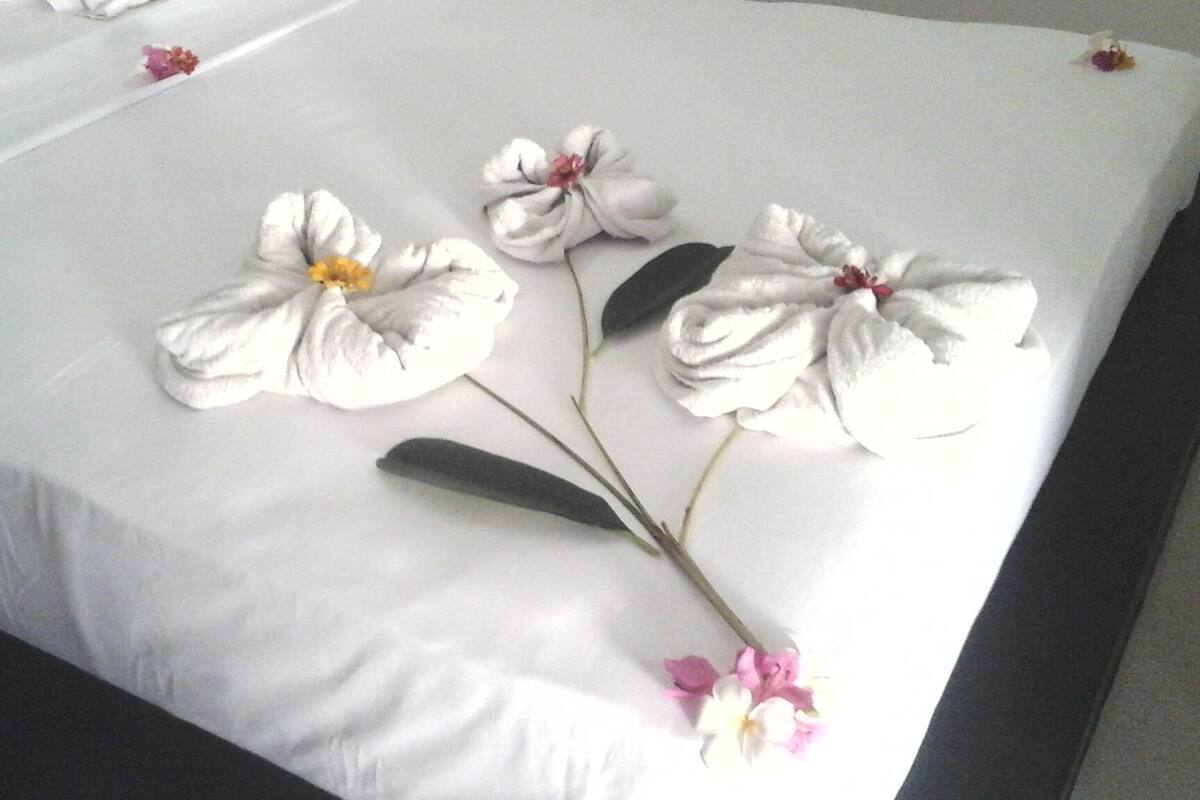 A neatly made bed with floral arrangements and a single rose petal.
