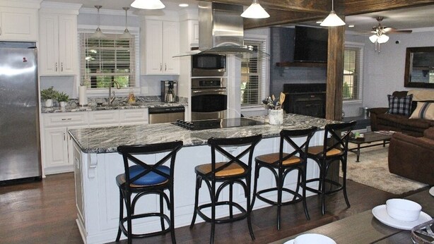 A modern kitchen with white cabinets, a large island with bar stools, stainless steel appliances, and pendant lighting. - Beautiful Rustic Murfreesboro Home just minutes from I24, MTSU and more (Murfreesboro)