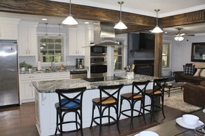 Una cocina moderna con armarios blancos, una isla grande con taburetes de bar, electrodomésticos de acero inoxidable e iluminación colgante.