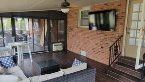 A spacious living area with a large sliding glass door leading to a patio, a comfortable sofa set, a flat-screen TV mounted on the wall, and a staircase with a black railing. - Beautiful Rustic Murfreesboro Home just minutes from I24, MTSU and more (Murfreesboro)