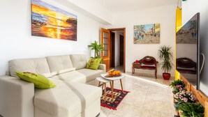 Una sala de estar con sofá, una mesita con fruta, televisión y obras de arte en las paredes.