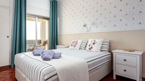 Una cama bien hecha con ropa de cama a rayas y cojines decorativos, una mesita de noche con una lámpara y una ventana con cortinas.