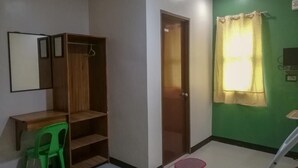 A room with a wooden wardrobe, a desk, a green chair, a door, and a green wall. - ROEXCIN Tourist Inn (Claver)