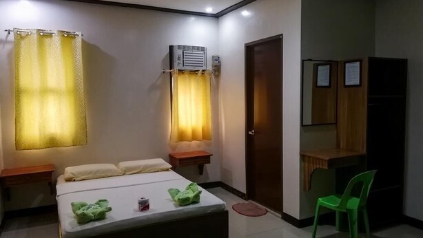 A hotel room with a bed, a desk, a chair, an air conditioning unit, and a door. - ROEXCIN Tourist Inn (Claver)
