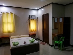 A hotel room with a bed, a desk, a chair, an air conditioning unit, and a door.