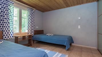 Une petite pièce simple, avec deux lits simples, un bureau et une fenêtre avec des rideaux.