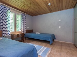 Une petite pièce simple, avec deux lits simples, un bureau et une fenêtre avec des rideaux.