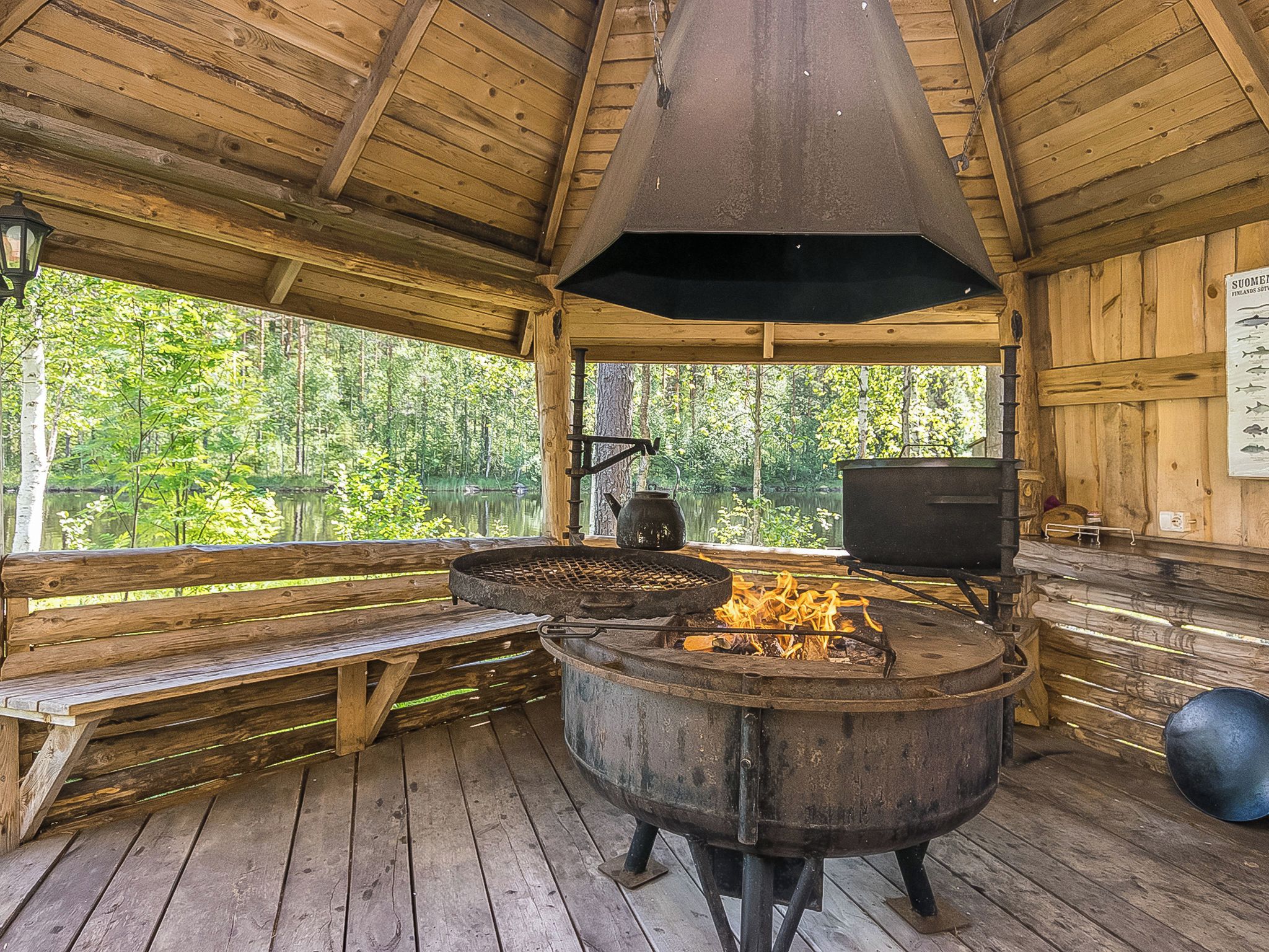Un rustico chalet in legno con un'ampia zona cottura esterna, una panchina e vista su una zona boschiva.