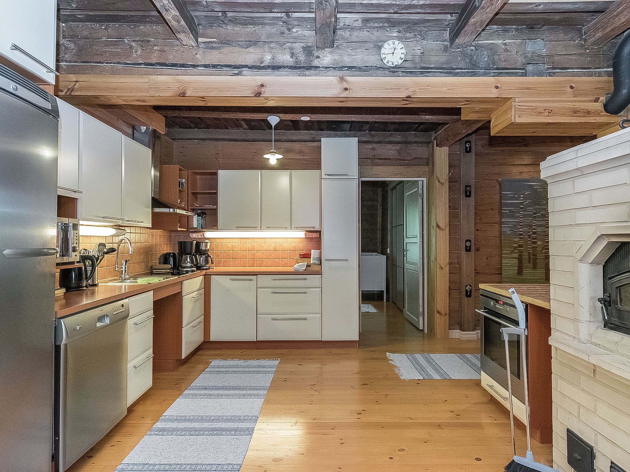 Une cuisine compacte dotée d’appareils électroménagers modernes, d’un plancher en bois et d’un plafond au style rustique.