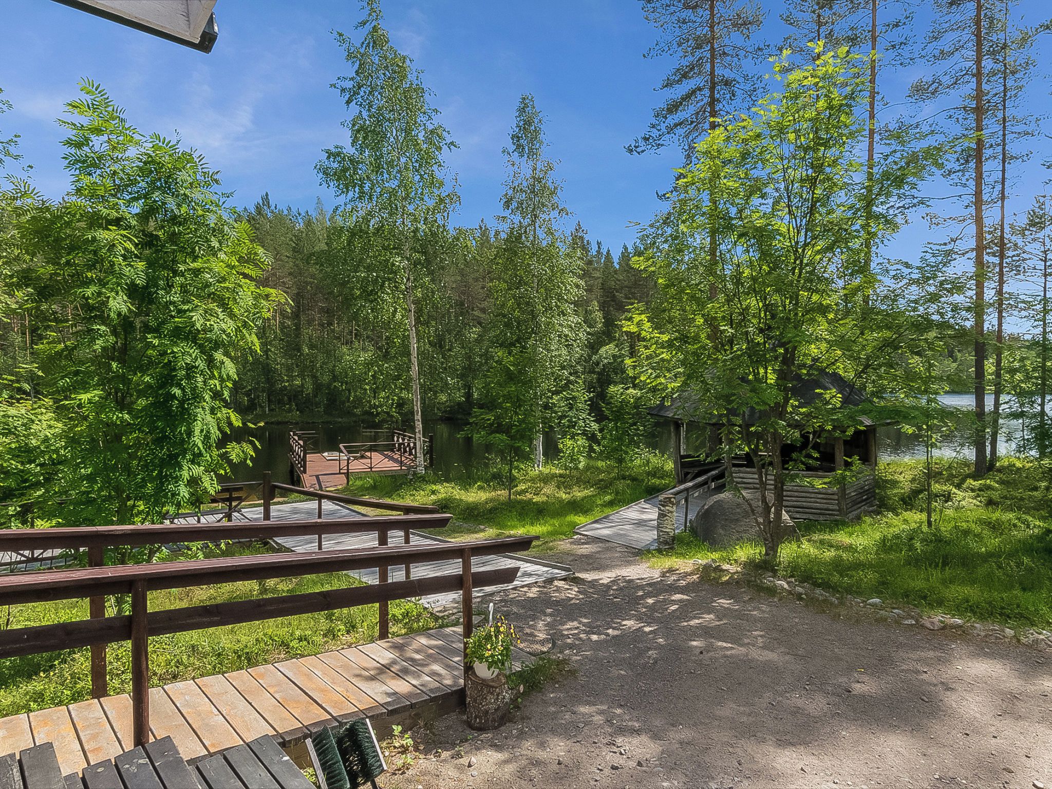 A wooden deck leading to a cabin with a view of a forest and a lake.