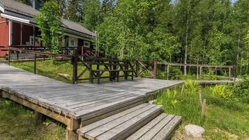 A wooden deck leading to a cabin with a metal railing, surrounded by dense forest.
