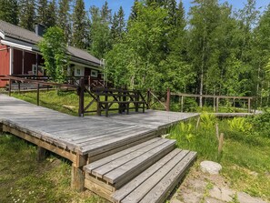 A wooden deck leading to a cabin with a metal railing, surrounded by dense forest.