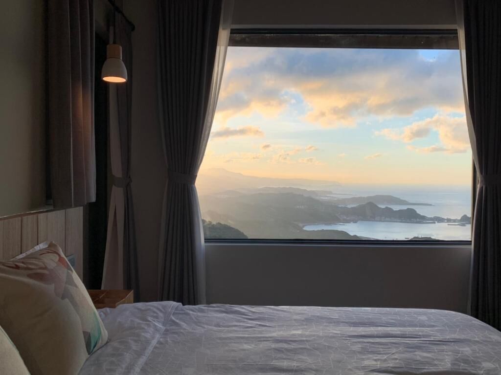 A hotel room with a large window offering a view of a coastal landscape during sunset.