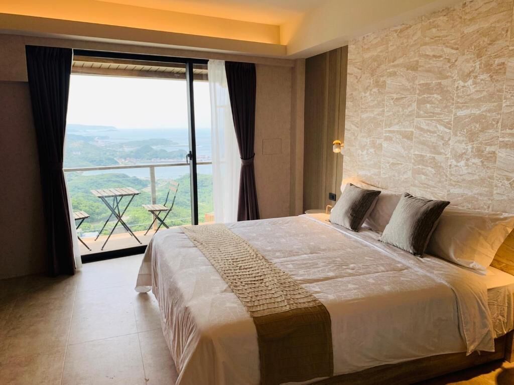 A bedroom with a large bed, a view of the outdoors, and a stone wall.