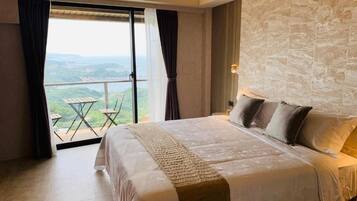 A bedroom with a large bed, a view of the outdoors, and a stone wall.