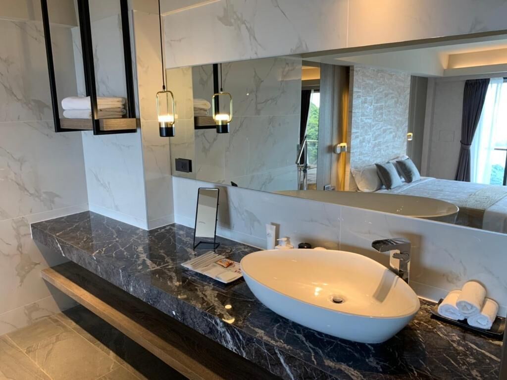 A modern bathroom with a large white sink, marble countertops, and a large mirror reflecting the room.