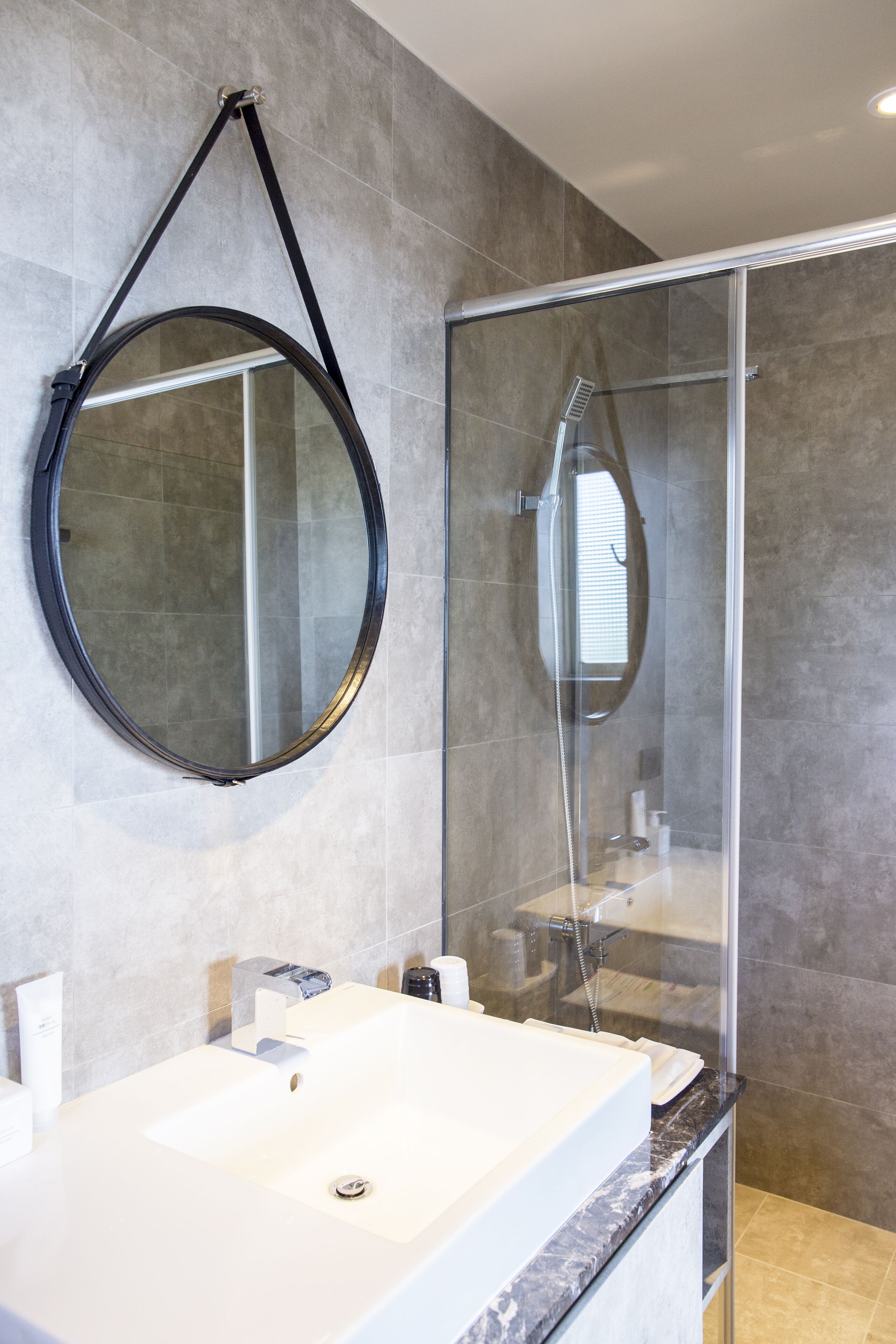 A modern bathroom with a large mirror, a glass-enclosed shower, and a white sink.