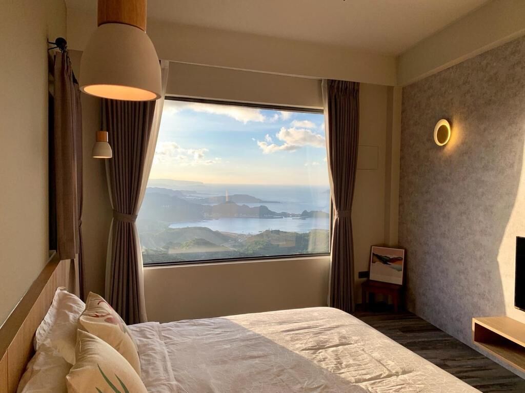 A hotel room with a large bed, a view of the sea, and a modern lamp.