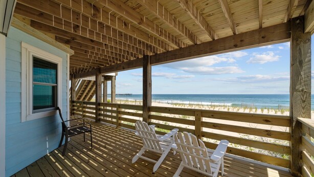 Una terraza de madera con dos sillas Adirondack blancas que dan a una playa.