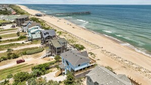 Una zona residencial costera con propiedades frente al mar, un muelle que se adentra en el océano y una playa de arena.