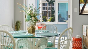 A dining area with a glass table and white wicker chairs, a wicker basket, and a vase with greenery. - ⚓5400 Gulf Dr! 55+ condo with amazing pool just steps away from the beach!⚓🏖 (Holmes Beach)