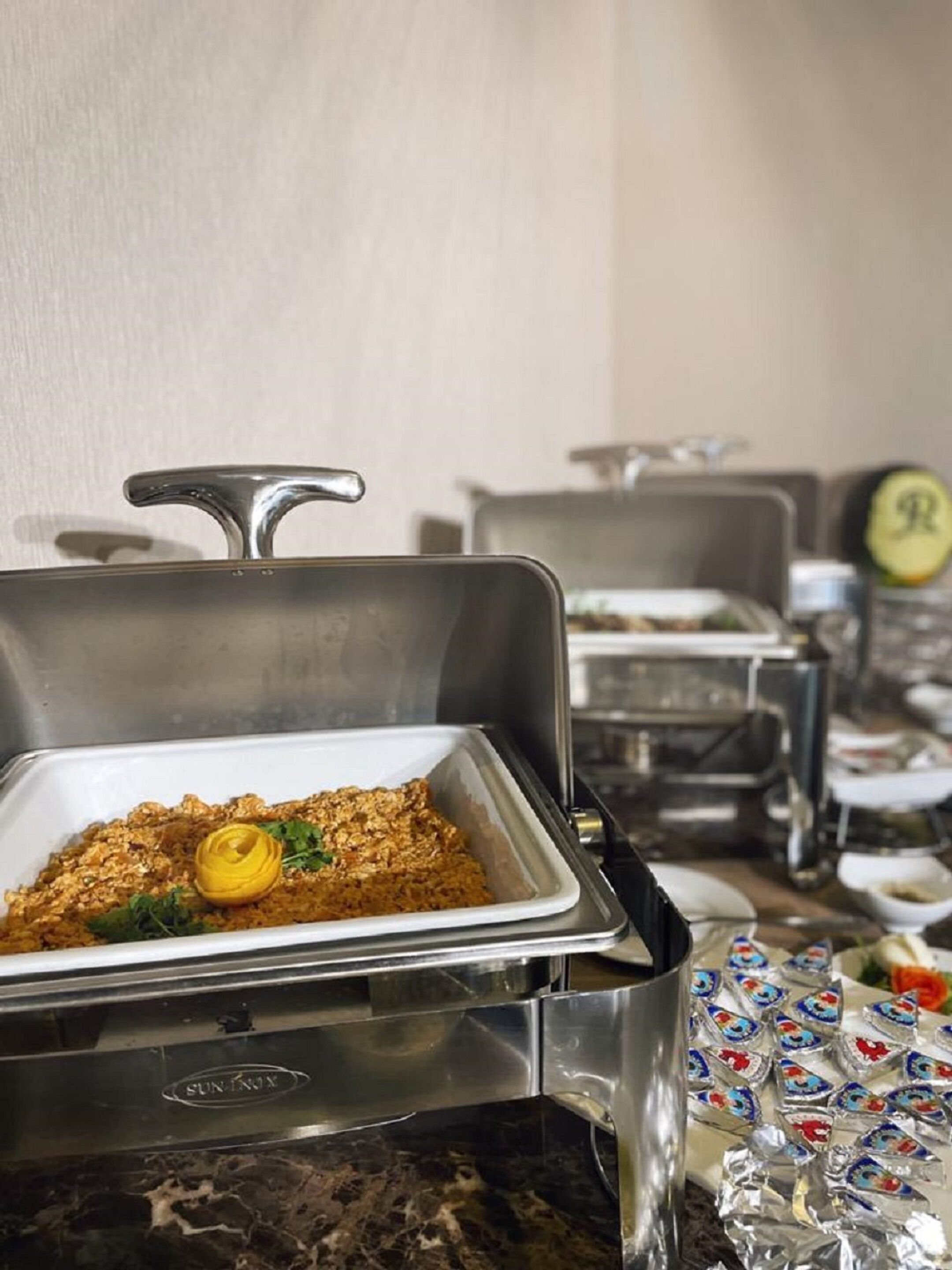 Un buffet avec un présentoir à nourriture couvert et divers récipients disposés à l’arrière-plan.