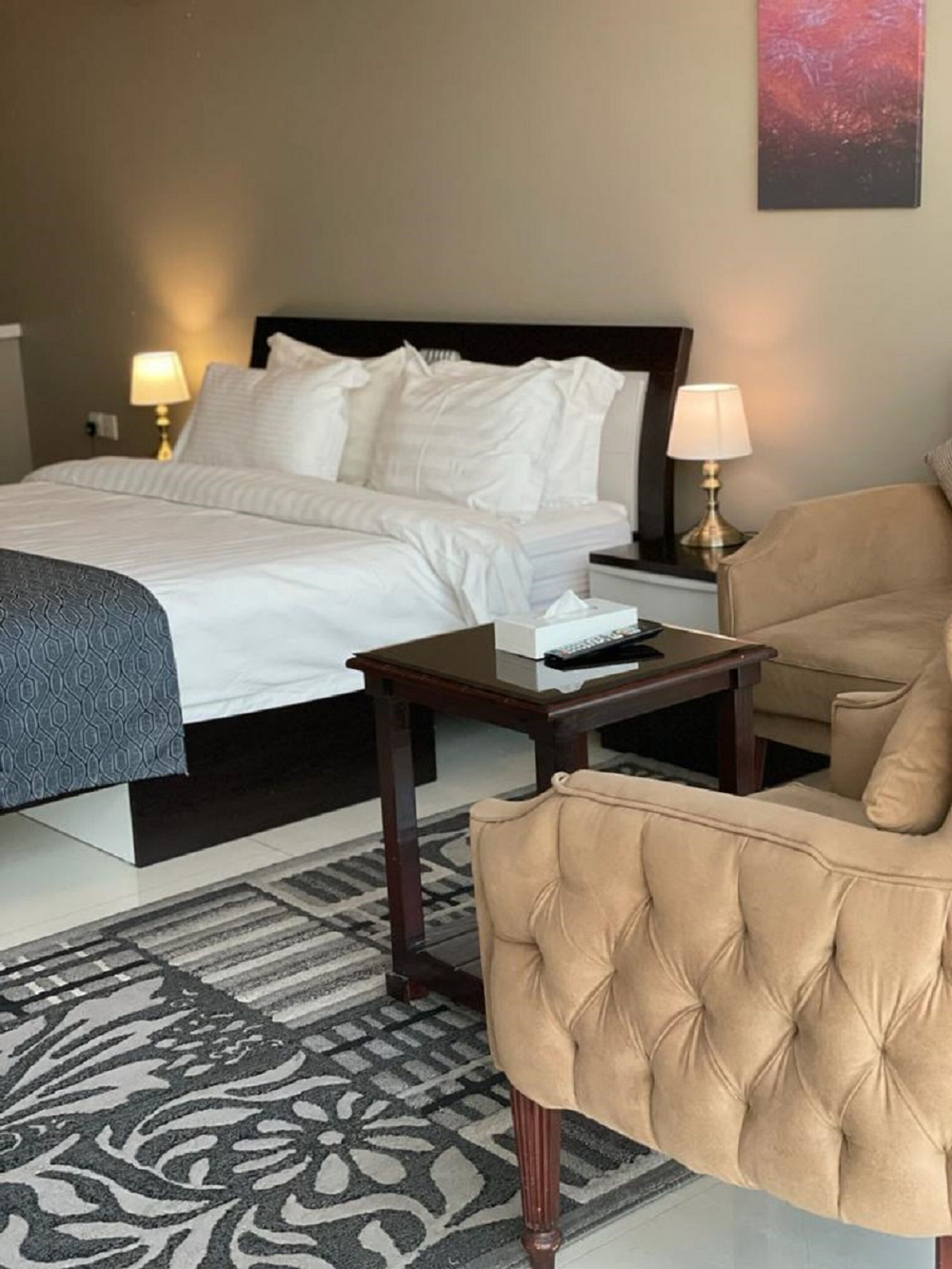 Quarto de hotel com cama, mesas de cabeceira, uma cadeira e um tapete.