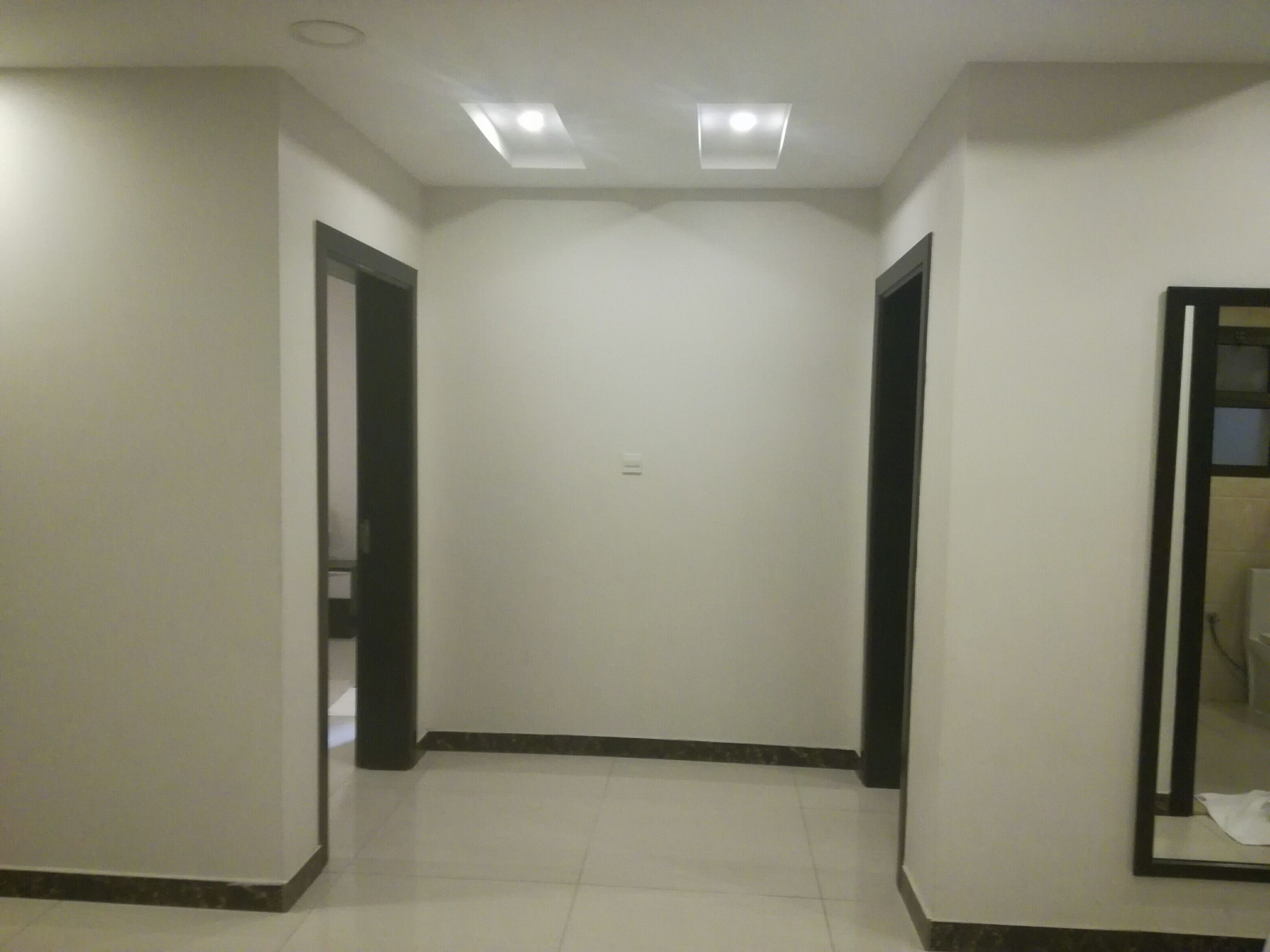 A hallway with white walls, a tiled floor, and two doors with black frames.
