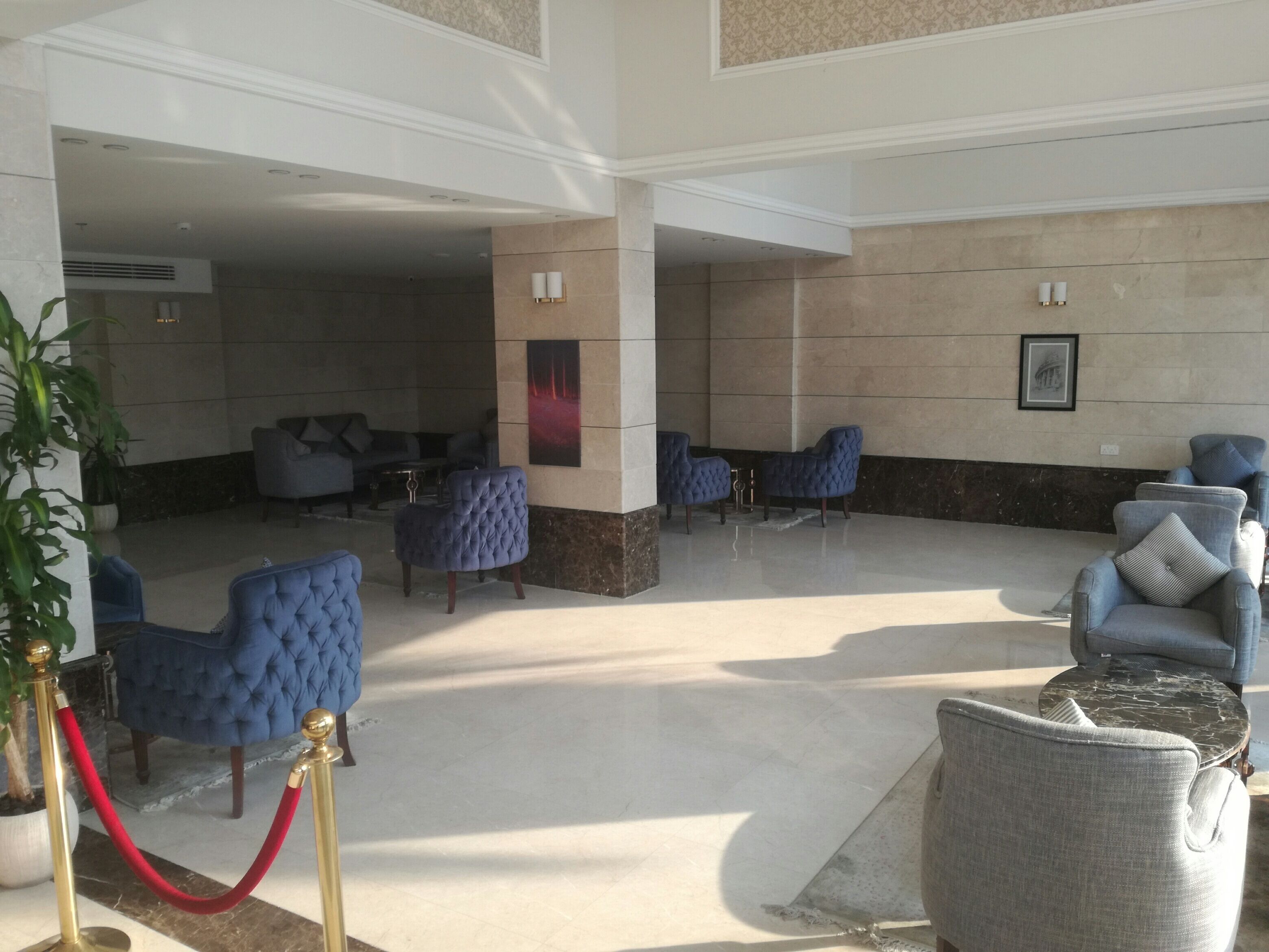 A lobby with a marble floor, blue upholstered chairs, a red rope barrier, and a framed picture on the wall.