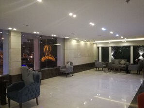 A modern lobby with a glass wall, a neon sign, and a seating area with sofas and armchairs. - Remaz Hotel & Suite (Al Jubail)