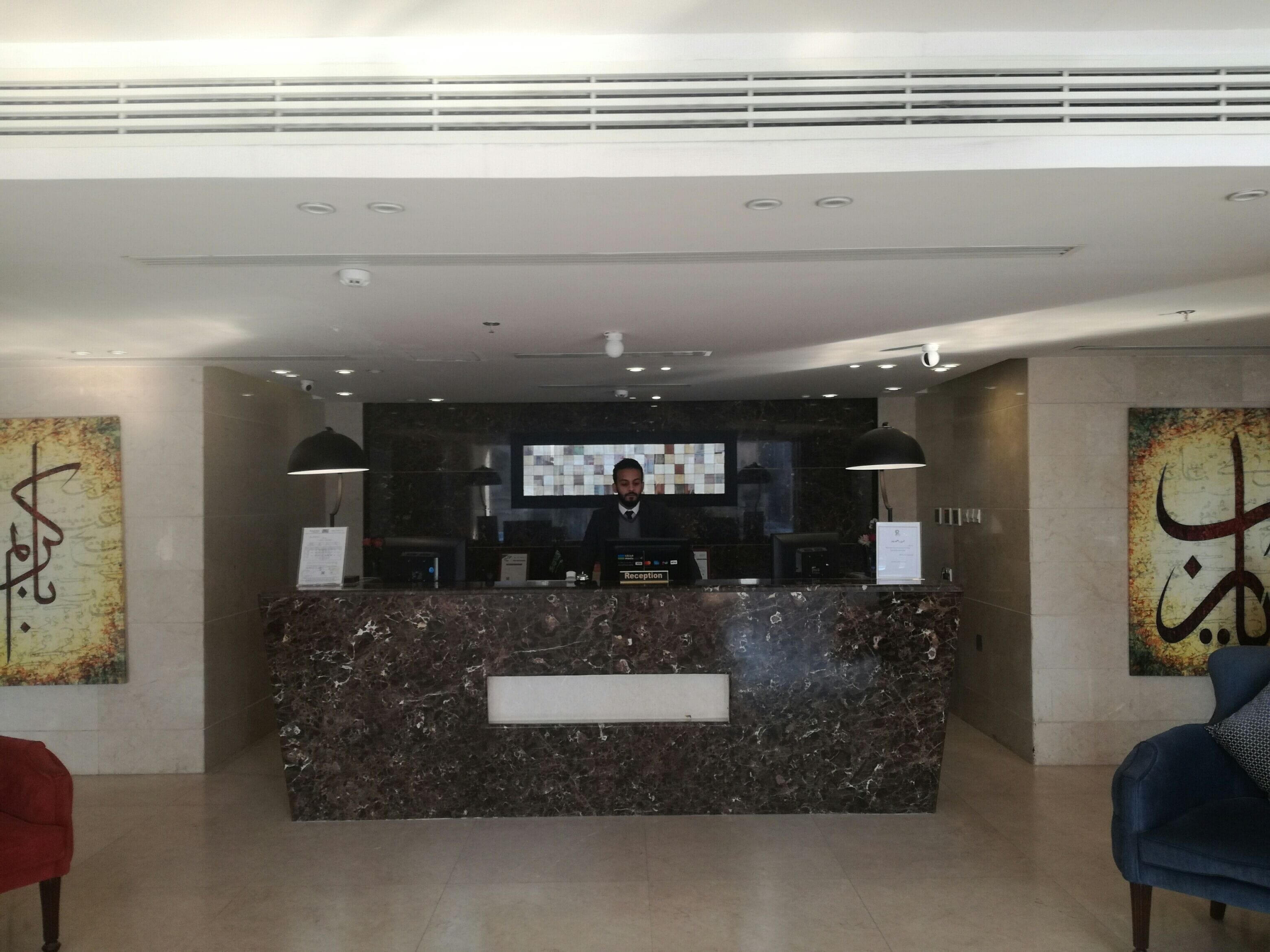 A reception desk with a marble counter, two pendant lights, and a digital screen above.