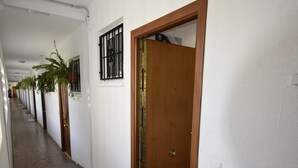 A hallway with doors numbered 15, a wooden door, a window with bars, and a plant.