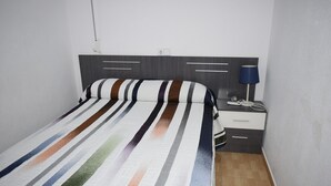 A neatly made bed with a striped bedspread, a bedside table with a lamp, and a wall socket.