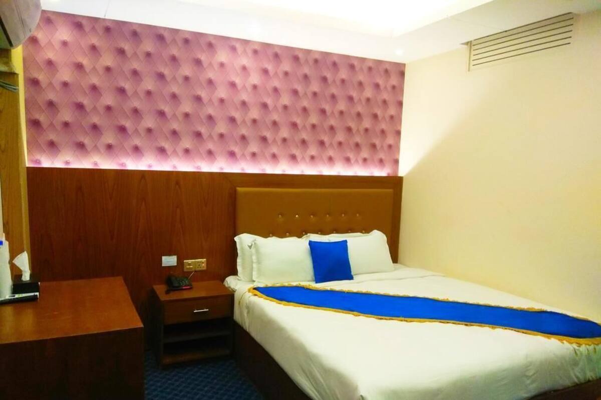 Ein Hotelzimmer mit einem Bett, einem Nachttisch aus Holz, einem Schreibtisch und einer Wand mit rosa Struktur.