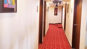 A hotel hallway with a red patterned carpet, white walls, and doors on both sides. - Hotel Grand View (Sylhet)