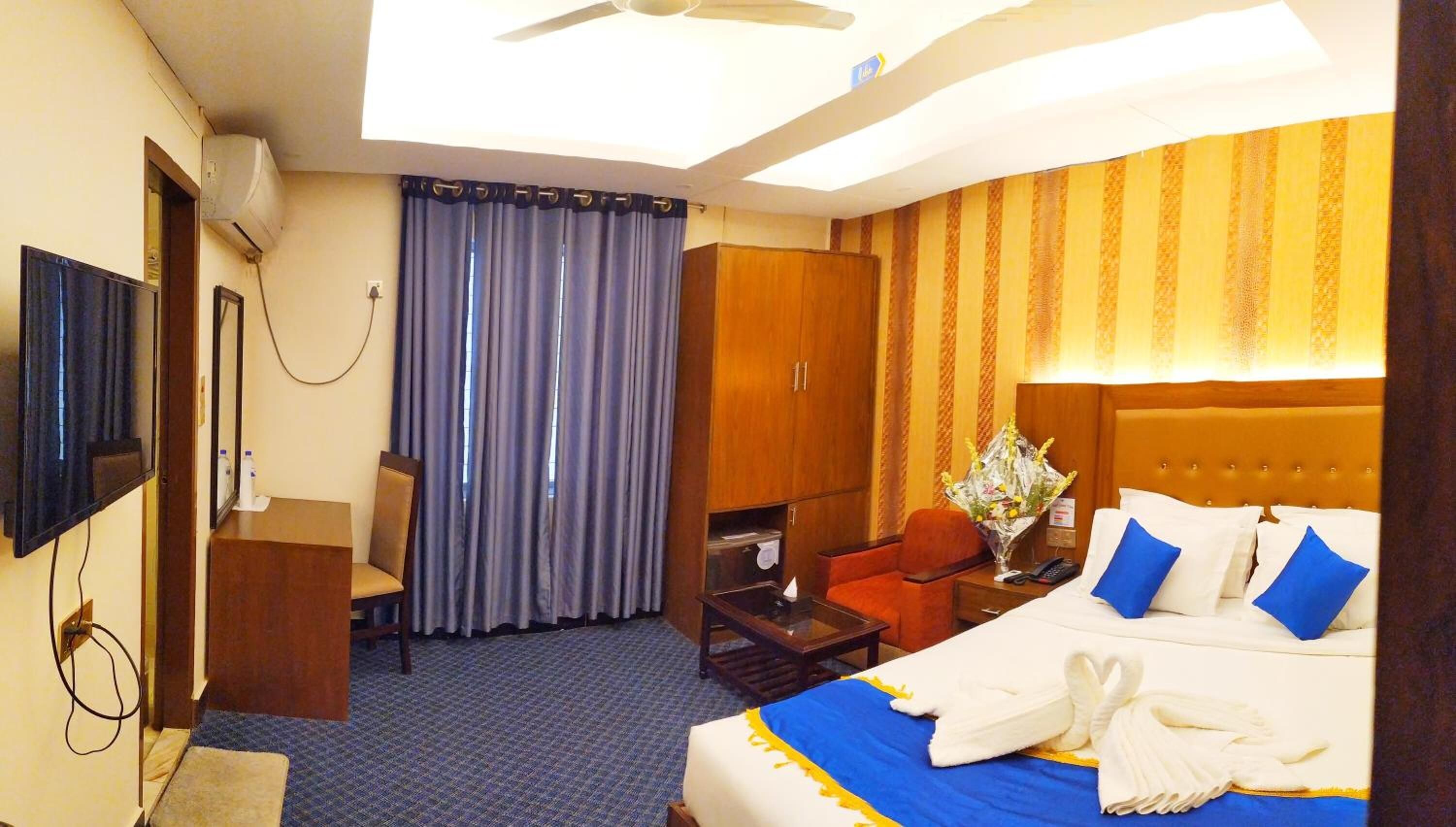 A hotel room with a bed, a desk, a chair, a TV, and a wardrobe.