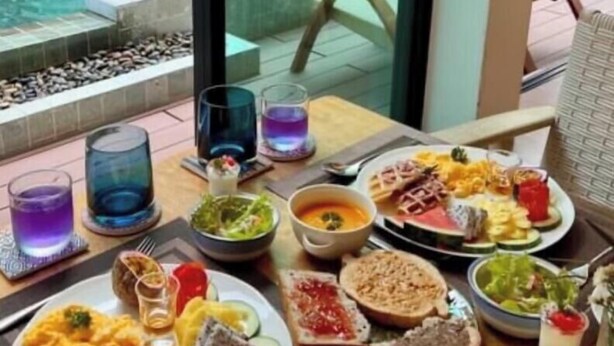 A dining table with various dishes, drinks, and cutlery, overlooking a pool and greenery. - Nine Hotel Chiangmai (Chiang Mai)