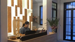 A reception desk with a modern design, a seated receptionist, and a potted plant. - Nine Hotel Chiangmai (Chiang Mai)