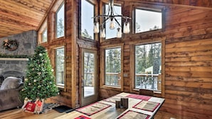 A cozy cabin interior with a wooden interior, a Christmas tree, a fireplace, and large windows offering views of the forest. - Luxury Mountain Getaway in Fairplay w/ Deck! (Fairplay)