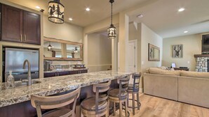 Una cocina con encimeras de granito, electrodomésticos de acero inoxidable y taburetes de bar de madera.