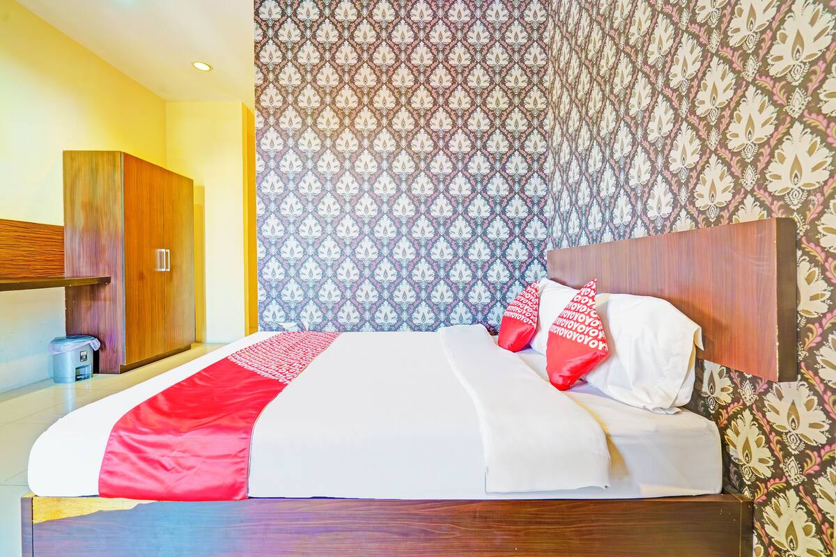 A hotel room with a bed, a wardrobe, and patterned wallpaper.
