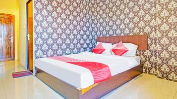 A neatly made bed with a wooden headboard, a patterned wallpaper, and a clean, tiled floor.