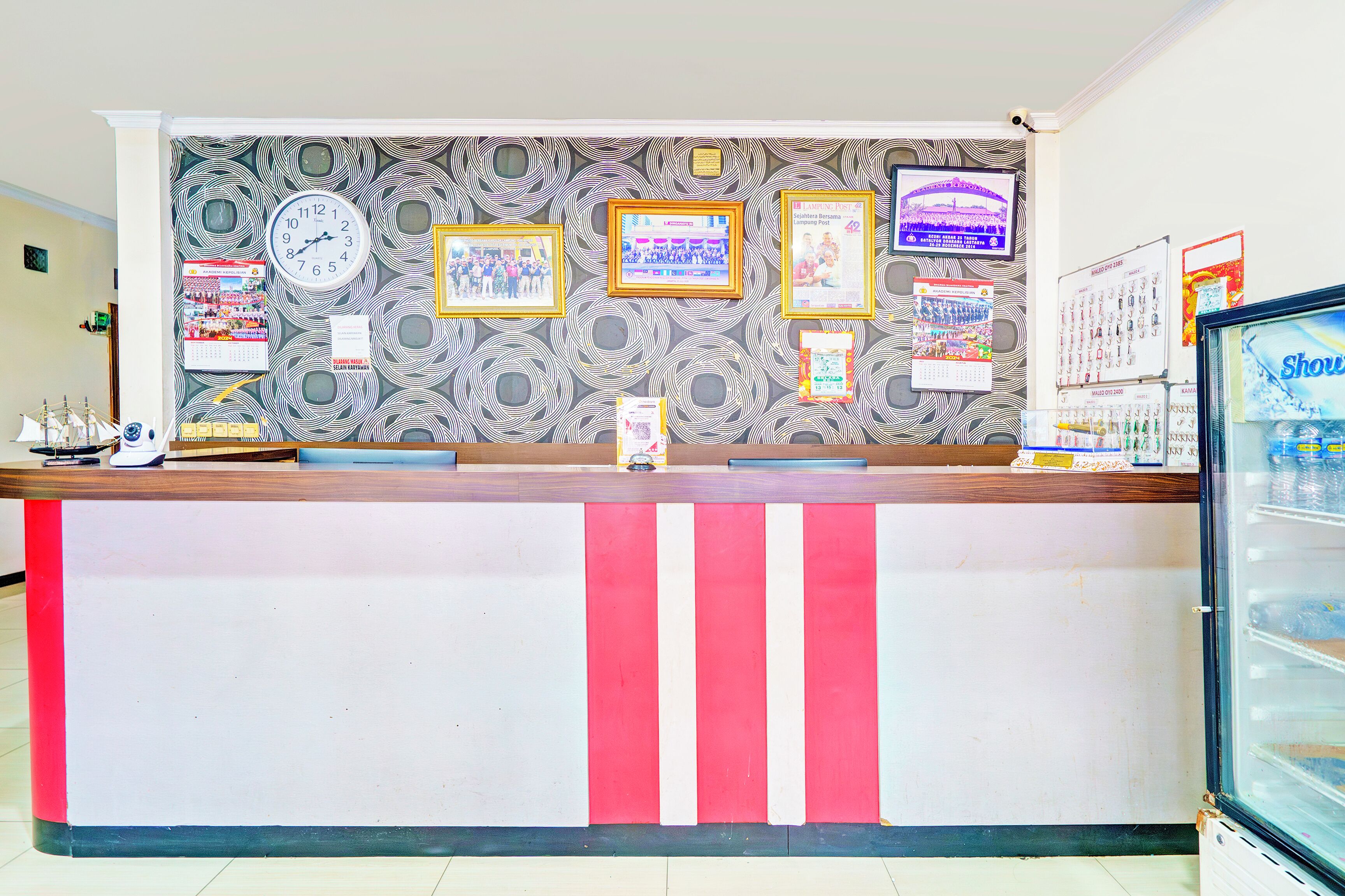 Un mostrador de recepción con papel tapiz estampado, un reloj, cuadros enmarcados y una pantalla digital.