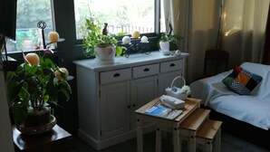 Une pièce comprenant un lit, une petite table, un bureau avec un ordinateur, une fenêtre avec des rideaux et une plante en pot.